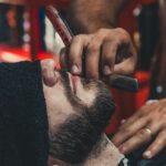 A barber skillfully shaves a man's beard using a straight razor at a barbershop.